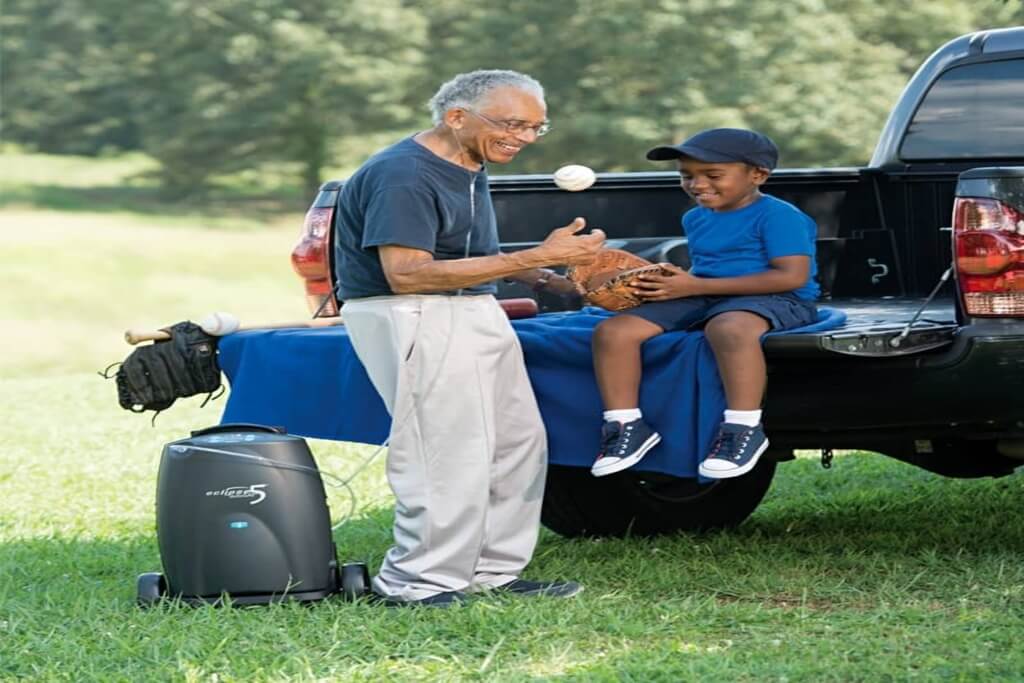 Smiling senior man wearing a nasal cannula, playing catch with a boy next to a portable oxygen concentrator