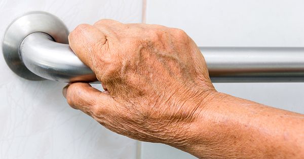 Older adult’s hand gripping a bathroom safety grab bar, showing how HHME bathroom aids improve safety and prevent falls