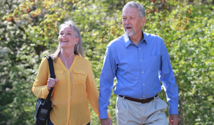 Older woman on portable oxygen therapy walking outdoors in Chicagoland, holding hands with partner, enjoying fresh air.