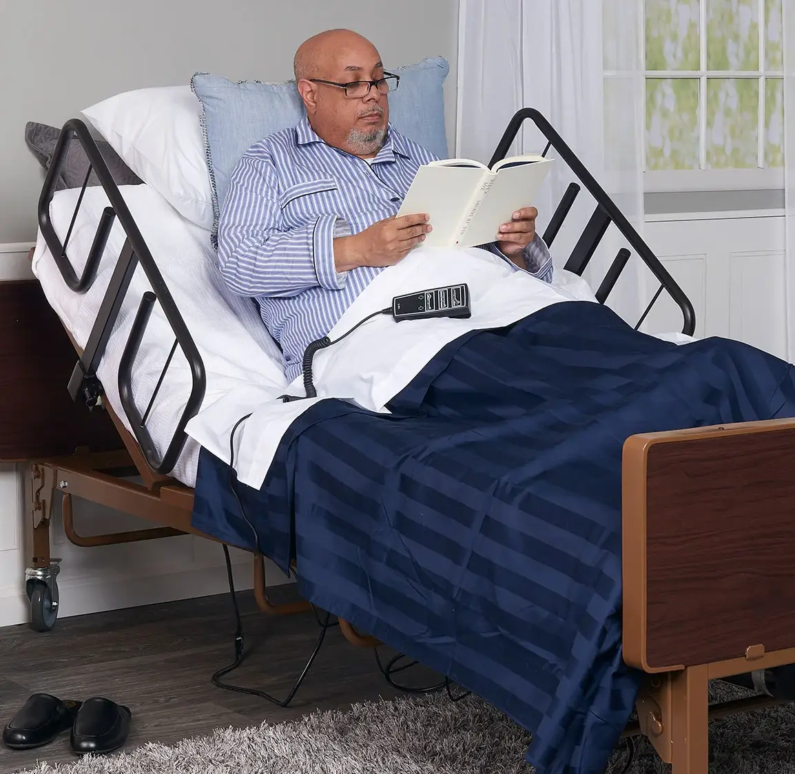 Man in pajamas reading a book in an adjustable hospital bed with side rails.