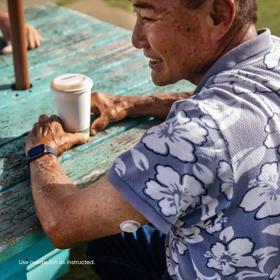 Man wearing a continuous glucose monitor sensor on his upper arm while sitting outside