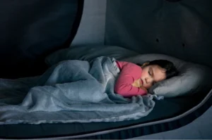 Close up of a young child in pink pajamas sleeping peacefully inside the Cubby Bed, protected by the enclosed safety walls.