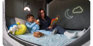 A smiling mother reading a book with her son inside the enclosed Cubby Bed, illustrating family engagement and sensory comfort.